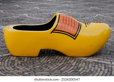 A large yellow Dutch wooden clog is displayed on a patterned stone surface - Powered by Shutterstock