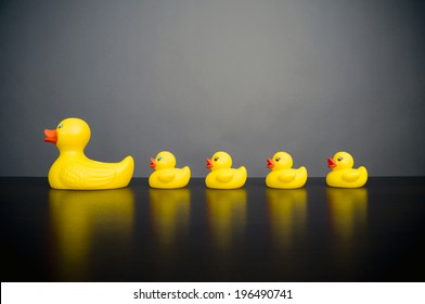 A Large Yellow Rubber Duck With Four Smaller Rubber Ducks In A Row Behind.