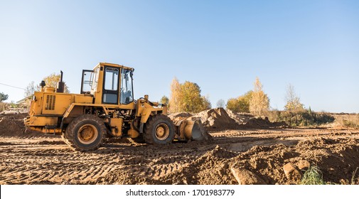 large yellow wheel loader aligns a piece of land for a new building. Preparation of the land for the auction. Leveling the landscape and adding sand for construction. Banner wallpaper.