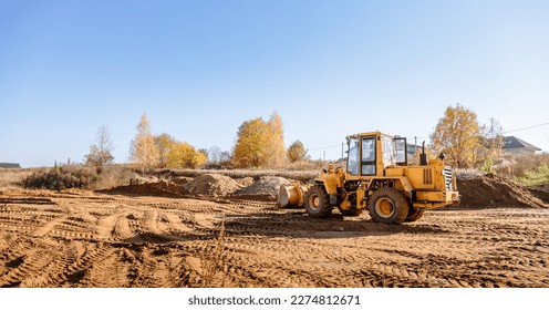 Large yellow wheel loader aligns plot of land for a new building. Land preparation for the auction. Leveling of territory and adding sand for construction site. Banner. Copy space. Special transport.