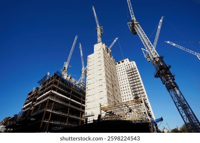 A large-scale construction site with multiple cranes erecting skyscrapers under a clear blue sky, symbolizing urban expansion and real estate growth