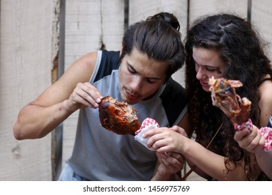 Larkspur, Colorado / USA - July 14, 2019:  A Young Couple, Man And Woman, Eating A Turkey Leg At The Colorado Renaissance Festival With A Man Bun
