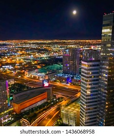 Las Vegas At Night With Millions Of Lights As Shot From A 57th Floor Balcony Shows This Cityscape Of Colorful Lights And Skyscrapers Under A Clear Sky With A Full Moon Shining Over This Active City