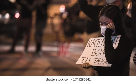 Las Vegas, NV, USA 5/30/2020 — An Asian woman wipes her tears holding a sign that reads, “Racism isn’t born. It’s taught.” Black Lives Matter protest in Downtown Las Vegas.