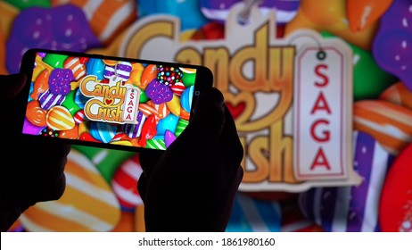 Las Vegas, USA, November 2020: Hold Your Smartphone In Hand To Play Candy Crush On A Blurred Background, A Large Screen With The Game Candy Crush Saga