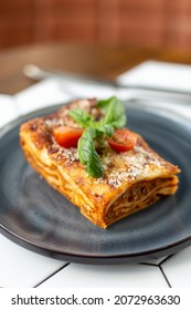 lasagna. Garnished with tomato and leaf. Against the background of a wooden table in a cafe