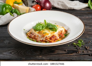 Lasagna with ground beef or minced pork and cheese, garnished with basil leaves and herbs. A hot main course of pasta, meat, cheese and herbs in a ceramic bowl on a wooden kitchen table.