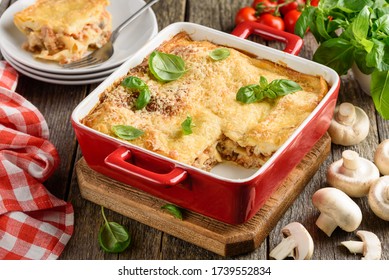 Lasagna with meat, mushrooms, tomatoes, cheese and bechamel sauce, decorated with basil in a red ceramic form. Traditional italian dish. Old wood background. Selective focus - Powered by Shutterstock