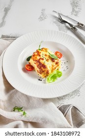 Lasagna With Tomato And Green Leaf. Fish With Bechamel Sauce. White Restaurant Plate On Light Table