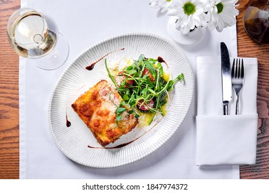 Lasagne Bolognese In A Plate And A Glass Of White Wine On A Table In A Restaurant. View From Above.