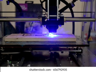 Laser engraving on wood macro. 3D printer laser beam burns the pattern close-up on a wooden board. Industrial Modern technological background. Laser blue 3d printer moves on a wooden surface