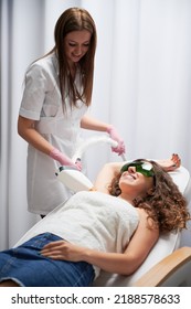 Laser skin care. Cosmetologist doing hair removal from axillary area of happy client. Young woman with smile expression liying on white couch and enjoying pleasant procedure of losing unwanted hair. - Shutterstock ID 2188578633