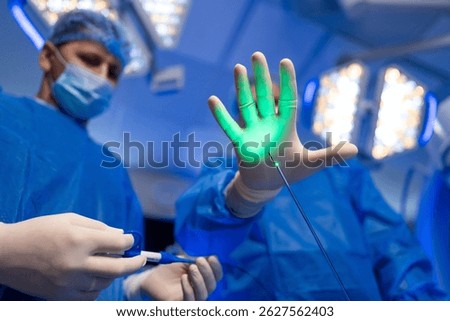 Laser surgery in operating room. Surgeons in blue scrubs are conducting a laser procedure, focusing on a patient's hand with a glowing green light.
