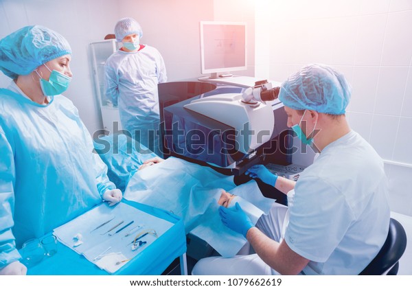Laser vision correction. A\
patient and team of surgeons in the operating room during\
ophthalmic surgery. Eyelid speculum. Lasik treatment. Patient under\
sterile cover
