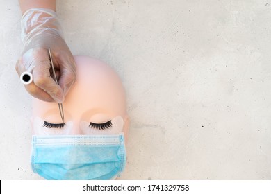 Lash Artist Theme Beauty Background.  Training Mannequin Head With Strip Lashes And Protective Mask.  Lash Artist Wearing Glue Ring Applying Lash Extensions.  Plain Background With Space.