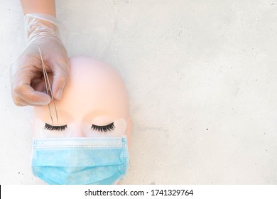 A Lash Artist Working On A Training Mannequin Head Wearing A Protective Mask.  Isolating Lashes In Lash Extension Treatment.  Top Down Beauty Background With Plain Background And Space For Copy Text