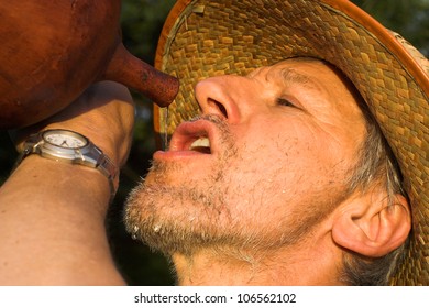 Last Drop Of Water Horizontal Image Made On Sweltering Late Afternoon To A Man Drinking Water From A Jug. He Is Beardy, Seems To Be Thirsty And Tired, And Wears A Straw Hut.