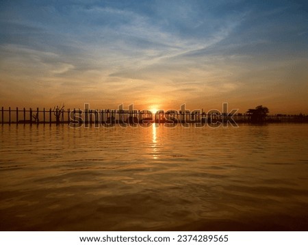 Last light at U Beng Bridge, wooden bridge in Mandalay, Myanmar, Wonderful orange sun set scenery with silhouette of people walking across the bridge with twilight sky background