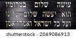 Last lines of Jewish prayer Kaddish on black wooden background. Translation is: He who creates peace in His celestial heights, may He create peace for us and for all Israel, and say, Amen