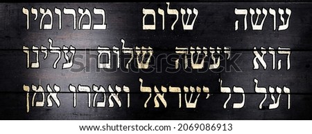 Last lines of Jewish prayer Kaddish on black wooden background. Translation is: He who creates peace in His celestial heights, may He create peace for us and for all Israel, and say, Amen
