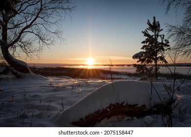 The last rays of the setting sun illuminate the snowy shore of the frozen river - Powered by Shutterstock