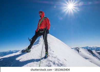 Last steps before Mont Blanc (Monte Bianco) summit 4,808m of smiling rope team man with climbing axe dressed mountaineering clothes,boots with crampons walking by snowy slopes with blue sky background