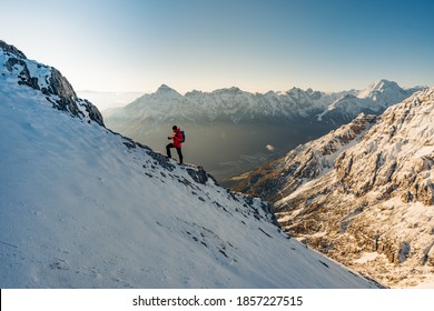 Last Steps Before Summit Mount Serles. Climber In A Red Jacket Climbs A Mountain Against A Blue Sky. Mountaineering Clothes, Boots With Crampons Walking By Snowy Slopes With Blue Sky Background.  