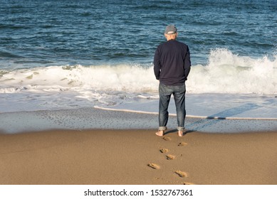 Late Afternoon Photo Of An Older Man (back Only) Standing On The Edge Of The Water Looking At The Ocean Waves On Cape Cod (Provincetown Massachusetts ).