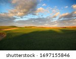 Late in the afternoon the sun is shining across the par 3 grass green on a golf course. Beautiful blue sky with clouds in the background, hover over the sand bunkers.