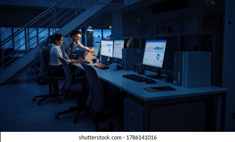 Late at Night In Modern Office: Businessman and Businesswoman Work on Desktop Computer, Having Discussion, Finding Problem Solution, Finishing Project. Successful Dedicated Responsible Office Workers