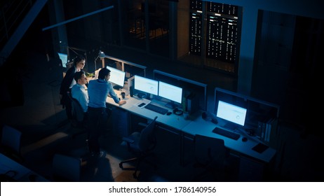 Late at Night In Modern Office: Diverse Team of Successful Businessmen and Businesswomen Gather Around Computer, Have Discussion, Find Problem Solution, Finishing Project Together. High Angle - Powered by Shutterstock