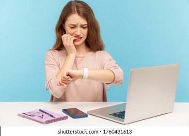 Too late, no time to meet deadline! Upset worried woman employee sitting at workplace and looking at wrist watch with anxiety, nervous about late hour. indoor studio shot isolated on blue background