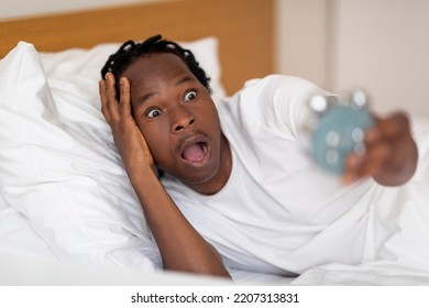 I'm Late. Overslept Black Man Looking At Alarm Clock With Shock, Emotional African American Male Lying In Bed In The Morning, Having No Time To Get Ready For Work, Closeup Portrait With Free Space