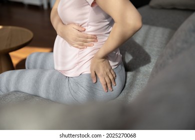 Late Pregnant Woman Suffering From Backache, Sitting On Couch, Holding Belly, Touching Back. Expectant Mother Tired Of Overweight, Having Health Problems, Feeling Lumbago Muscles Pain. Cropped Shot