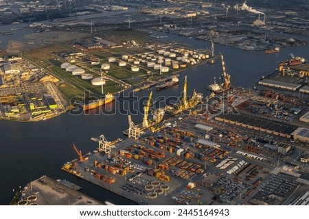 Late sunsets aerial view of Amsterdam harbour or port, with docks, cranes, shipping containers on shore. Canal and waterways leading towards the city in last ray of sunshine