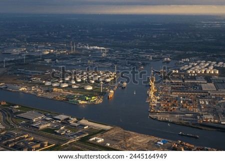 Late sunsets aerial view of Amsterdam harbour or port, with docks, cranes, shipping containers on shore. Canal and waterways leading towards the city in last ray of sunshine