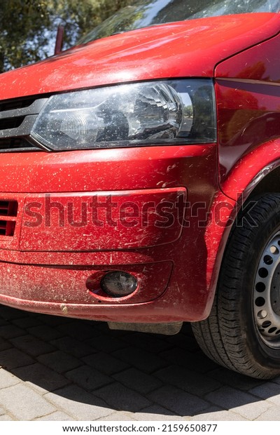 Lateral font part of a parked red\
van, covered in mud and dust. The car needs to be\
cleaned