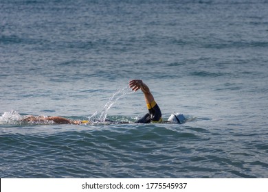 Lateral View Of A Woman Swimming In Open Water With Crawl Style. She Is Wearing A White Swimming Cap, And A Swimming Suit