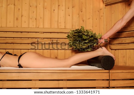 lateral view of a young woman having a russian sauna procedure with bath brooms from oak leaves
