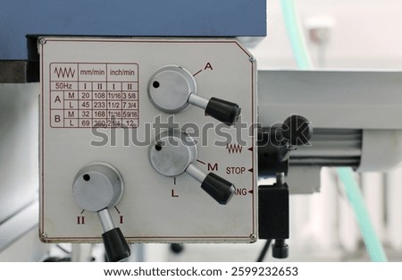 Lathe machine control panel. A close-up of a lathe machine control panel with feed adjustment levers. The panel displays a feed rate chart in millimeters and inches per minute.