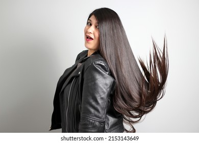 Latin Adult Real Woman With Long Straight Black Hair That Flies In The Air Is Content And Happy With Her Body Wearing A Black Leather Jacket	