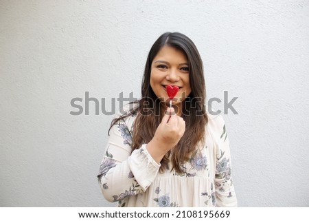 Latin adult woman with red heart-shaped lollipops to show her enthusiasm for the arrival of February and celebrate and show her affection on Valentine's Day of Love and Friendship with her family, fri