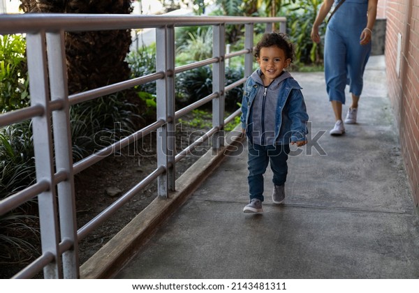 Latin\
American boy walks alone in front of his mother. He smiles at the\
camera. Concept going for a walk,\
motherhood
