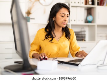 Latin American businesswoman sitting in office at workplace and working at laptop