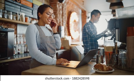 Latin American Coffee Shop Employee Accepts a Pre-Order on a Mobile Phone Call and Writes it Down on Laptop Computer in a Cozy Cafe. Restaurant Manager Browsing Internet and Talking on Smartphone. - Shutterstock ID 1882428598