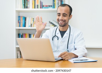 Latin American Doctor Greeting Patient At Video Call At Computer At Hospital