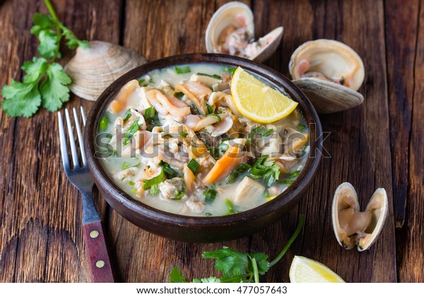 Latin American food. Seafood shellfish ceviche raw\
cold soup salad of seafood shellfish almejas, lemon, cilantro onion\
in clay bowl on wooden background. Traditional dish of Peru or\
Chile