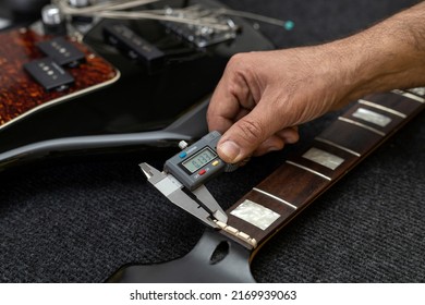 Latin American luthier measures the thickness of an electric bass capo with a digital vernier. Unrecognizable. Bass concept, calibration, instrument.