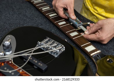 Latin American luthier takes accurate measurements of the distance of the frets of an electric bass with a digital vernier. Unrecognizable person. Bass concept, calibration, instrument.