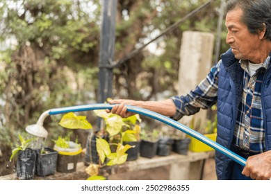 Latin american male gardener watering plants with a hose in a nursery on a sunny day - Powered by Shutterstock